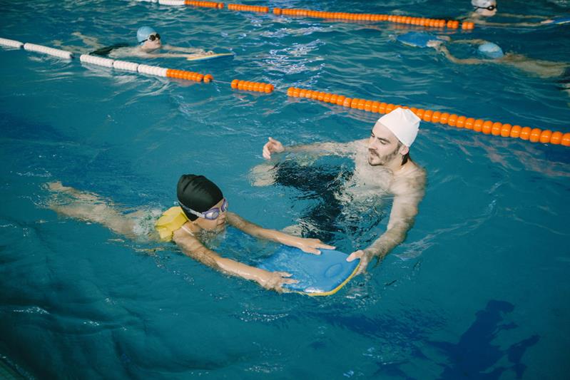 coach teaching kid in indoor swimming pool