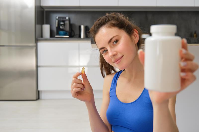 woman fitness instructor showing bottle of vitamins