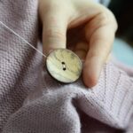 workers' hands sew a wooden button to a jacket.