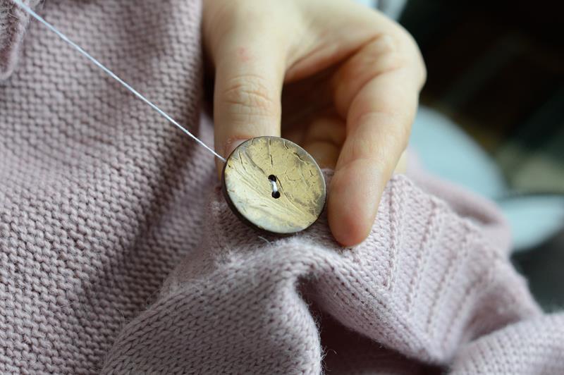 workers' hands sew a wooden button to a jacket.