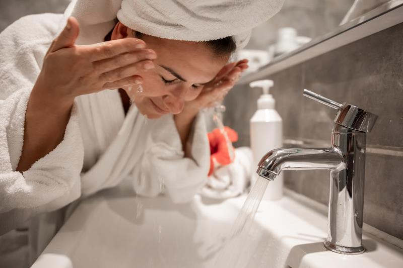 young woman in the bathroom washes her face with tap water